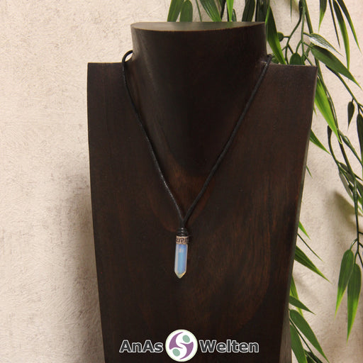 Das Bild zeigt einen Opalglas Stift-Anhänger klein mit Kette. Der Stift-Anhänger ist halbdurchsichtig und schimmert je nach Lichteinfall in einer weißen, blauen und/oder roten Farbe schimmert. Am oberen Ende verbindet ein silberfarbenes Element den Edelstein mit der Stoffkordel.