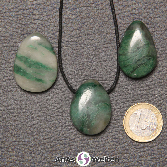 Drei grün-weiße Prasem gebohrte Trommelsteine nebeneinander. Einer befindet sich an einem schwarzen gewachsten Baumwollband.