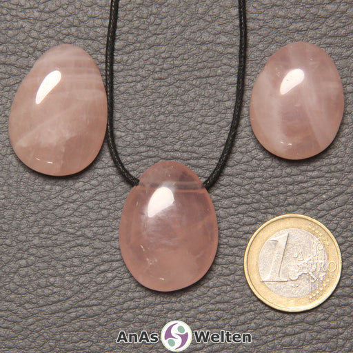 Drei rosa Rosenquarz gebohrte Trommelsteine nebeneinander. Einer befindet sich an einem schwarzen gewachsten Baumwollband.