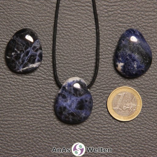 Drei blau-weiße Sodalith gebohrte Trommelsteine nebeneinander. Einer befindet sich an einem schwarzen gewachsten Baumwollband.