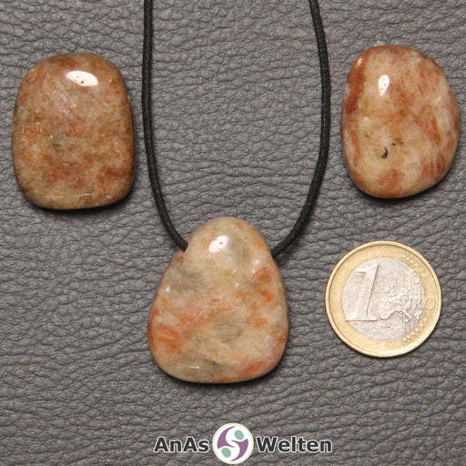 Drei rot-gelb-braune Sonnenstein gebohrte Trommelsteine nebeneinander. Einer befindet sich an einem schwarzen gewachsten Baumwollband.