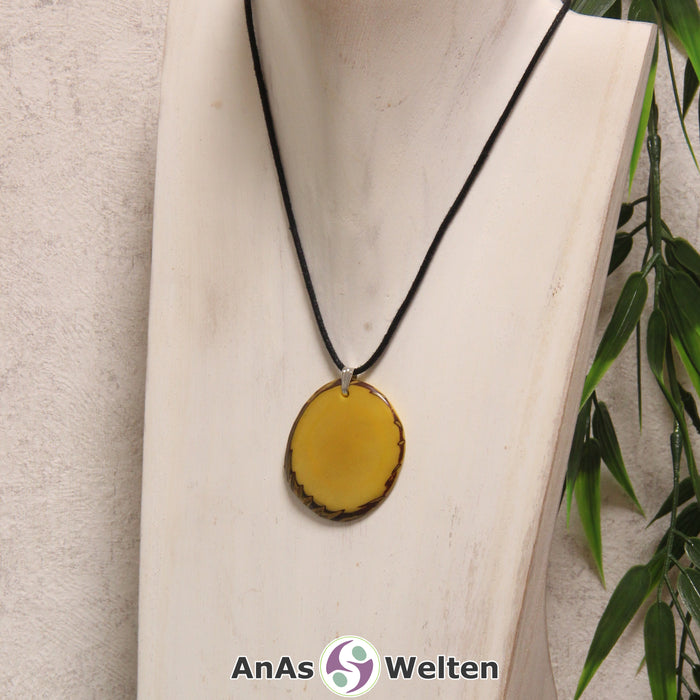 Eine gelb gefärbte Tagua-Nuss Schmuck Kette mit Öse mit einem schwarzen Baumwollband an einer hellen Büste.