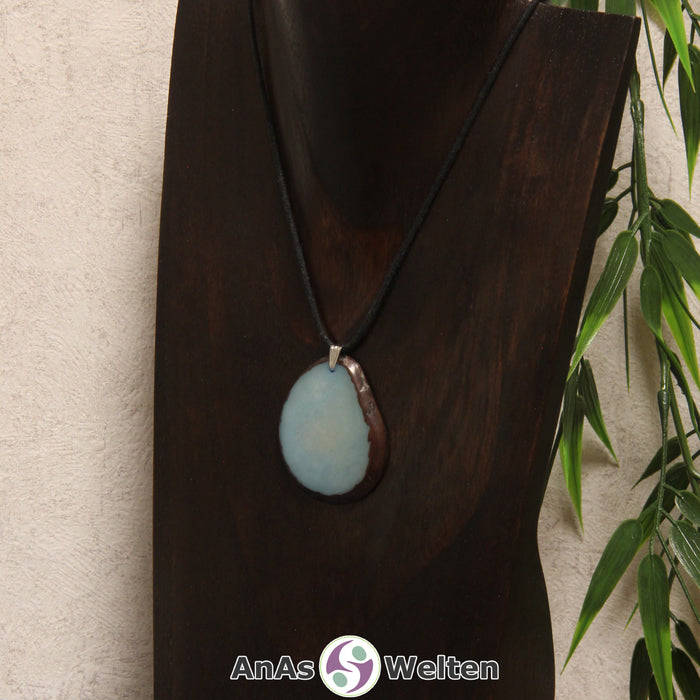 Eine himmelblaue Tagua-Nuss Schmuck Kette mit Öse mit einem schwarzen Baumwollband an einer dunklen Büste.