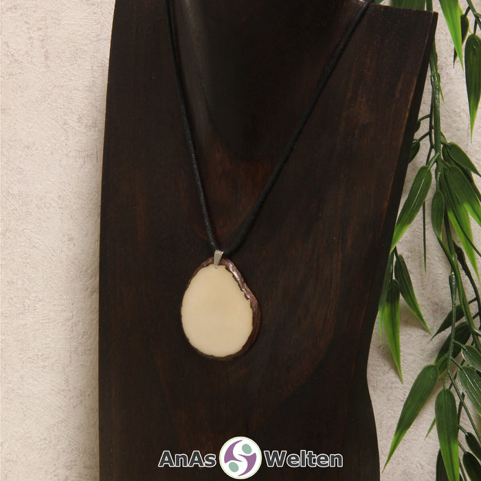 Eine naturfarbene Tagua-Nuss Schmuck Kette mit Öse mit einem schwarzen Baumwollband an einer dunklen Büste.