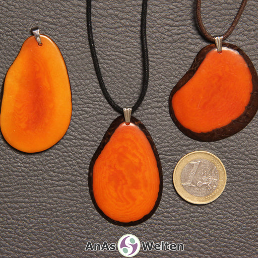 Drei orange gefärbte Tagua-Nuss-Scheiben mit Metallöse. Zwei sind an einem schwarzen bzw. braunen Baumwollband.