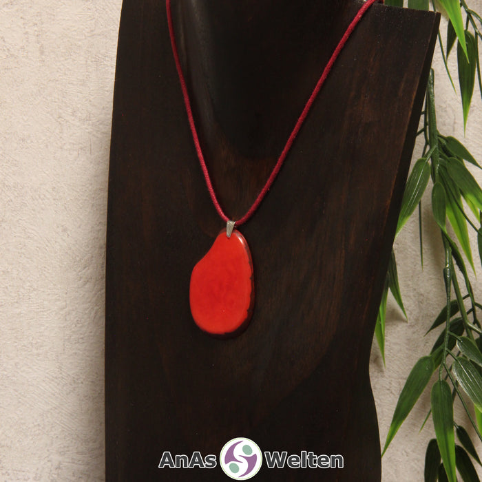 Eine rote Tagua-Nuss Schmuck Kette mit Öse mit einem roten Baumwollband an einer dunklen Büste.