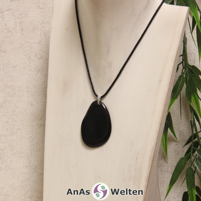 Das Produktbild zeigt die Tagua-Nuss-Schmuck Kette schwarz. Zu sehen ist eine schwarze Tagua-Nuss-Scheibe, die mit einer Edelstahlöse an einem schwarzen Baumwollband befestigt ist. Die Nuss-Scheibe hat einen dunklen Rand und eine glänzende Oberfläche.