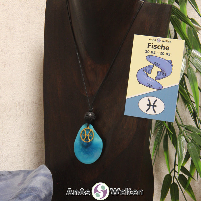 Eine türkis gefärbte Tagua-Nuss Sternzeichen Kette mit goldfarbenem Fische-Symbol und Lavakugel an einer dunklen Büste.