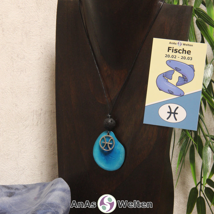 Eine türkis gefärbte Tagua-Nuss Sternzeichen Kette mit silberfarbenem Fische-Symbol und Lavakugel an einer dunklen Büste.
