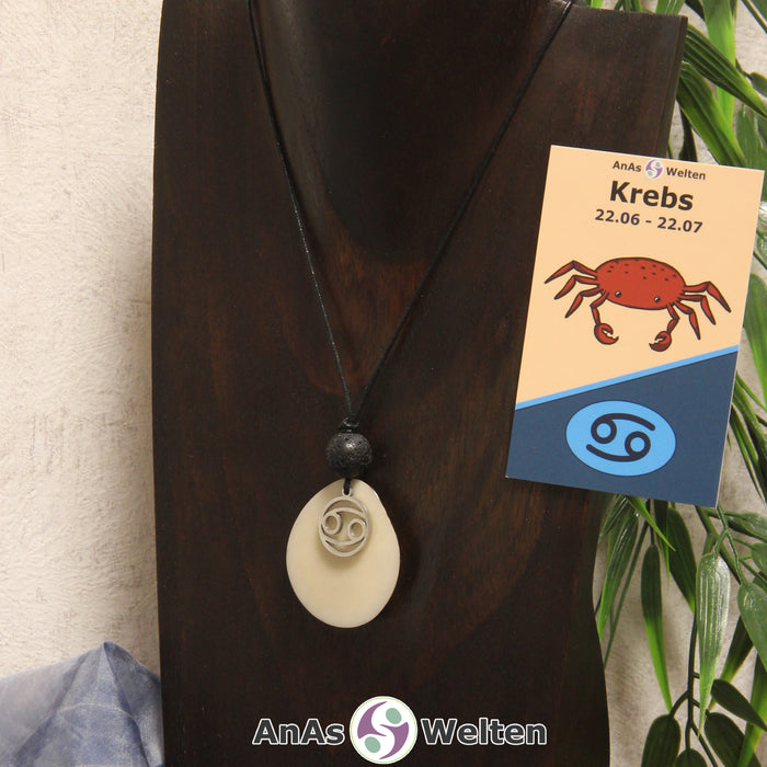Eine naturfarbene Tagua-Nuss Sternzeichen Kette mit silberfarbenem Krebs-Symbol und Lavakugel an einer dunklen Büste.