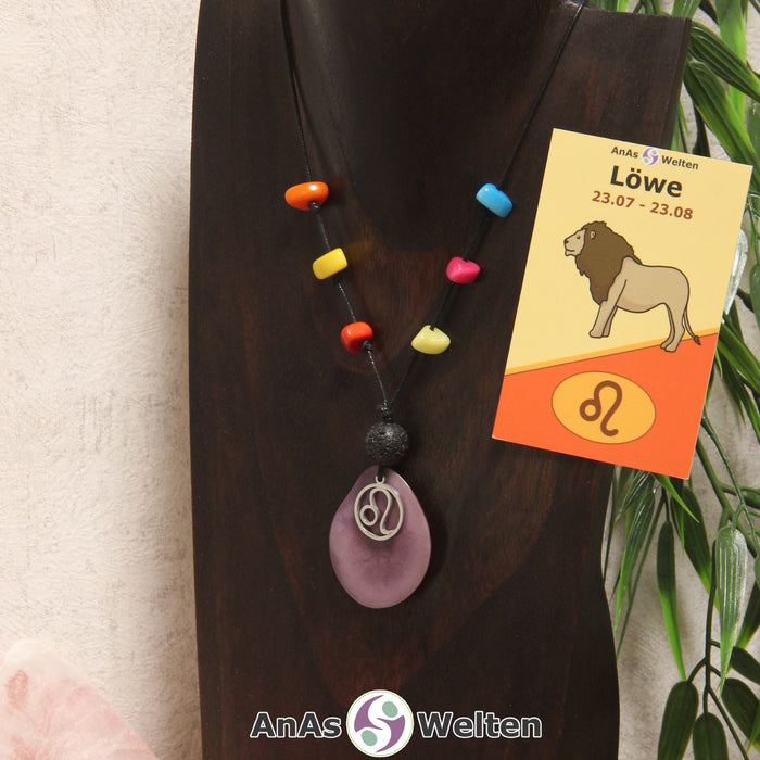 Eine lila Tagua-Nuss Sternzeichen Kette mit bunten Taguasplittern, silber Löwe-Symbol und Lavakugel an einer dunklen Büste.