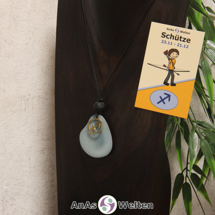 Eine himmelblau gefärbte Tagua-Nuss Sternzeichen Kette mit goldfarbenem Schütze-Symbol und Lavakugel an einer dunklen Büste.