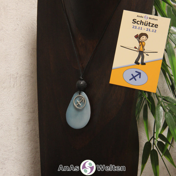 Eine himmelblau gefärbte Tagua-Nuss Sternzeichen Kette mit silberfarbenem Schütze-Symbol und Lavakugel an einer dunklen Büste.