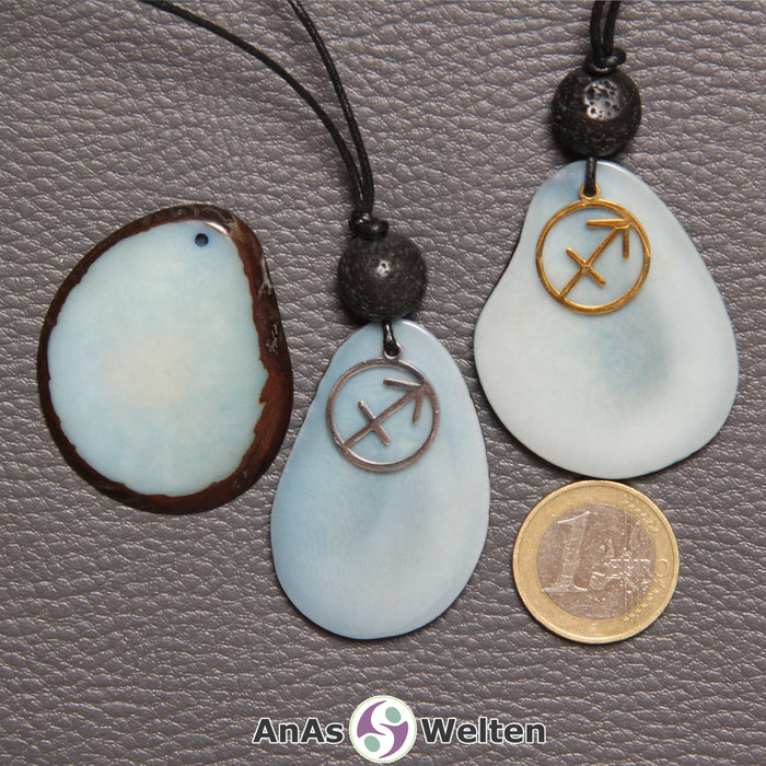 Drei Tagua-Nuss-Scheiben in himmelblau. Zwei davon sind als Kette mit Lavakugel und Schütze-Symbol gebunden.