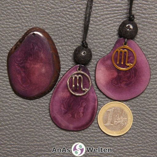 Drei Tagua-Nuss-Scheiben in violett. Zwei davon sind als Kette mit Lavakugel und Skorpion-Symbol gebunden.