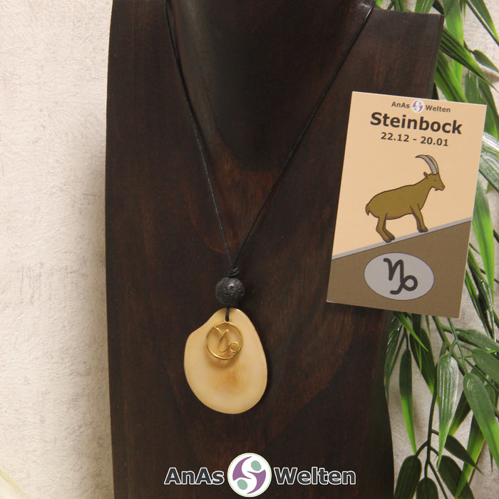 Eine beige gefärbte Tagua-Nuss Sternzeichen Kette mit goldfarbenem Steinbock-Symbol und Lavakugel an einer dunklen Büste.