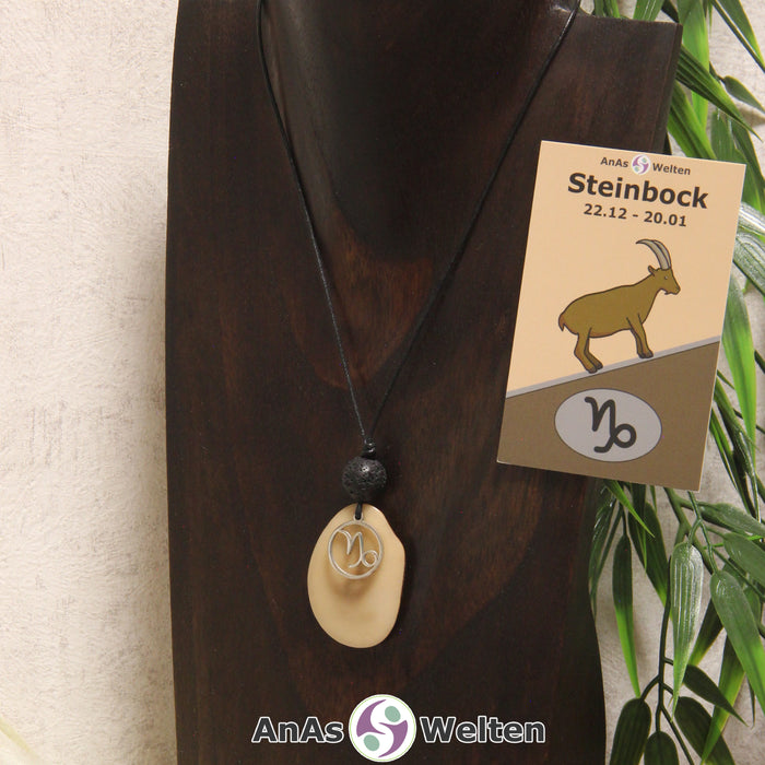 Eine beige gefärbte Tagua-Nuss Sternzeichen Kette mit silberfarbenem Steinbock-Symbol und Lavakugel an einer dunklen Büste.