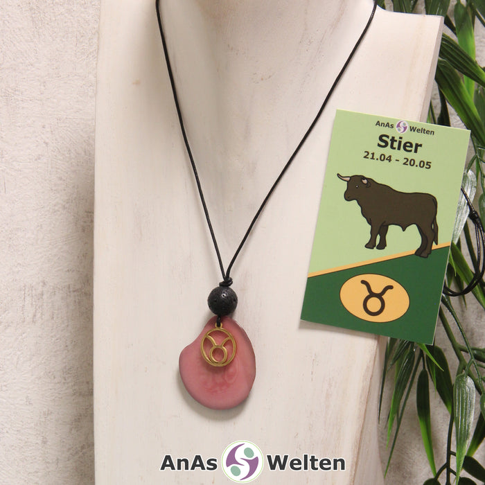 Eine rosa gefärbte Tagua-Nuss Sternzeichen Kette mit goldfarbenem Stier-Symbol und Lavakugel an einer hellen Büste.