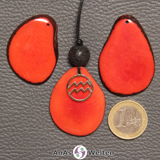 Drei Tagua-Nuss-Scheiben in rot. EIne davon ist als Kette mit Lavakugel und Wassermann-Symbol gebunden.