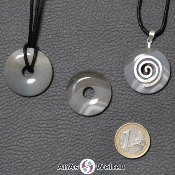 Drei Achat Donuts nebeneinander. Einer an einem Baumwollband, ein anderer an einem Donut-Halter mit Baumwollband.