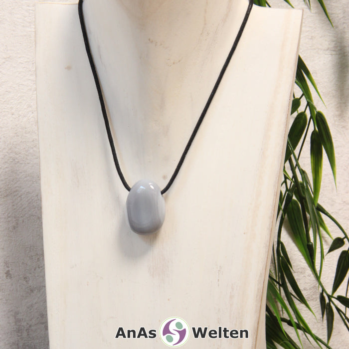 Ein grau-weißer Achat gebohrter Trommelstein an einem schwarzen Baumwollband, der um eine helle Büste gehängt wurde.