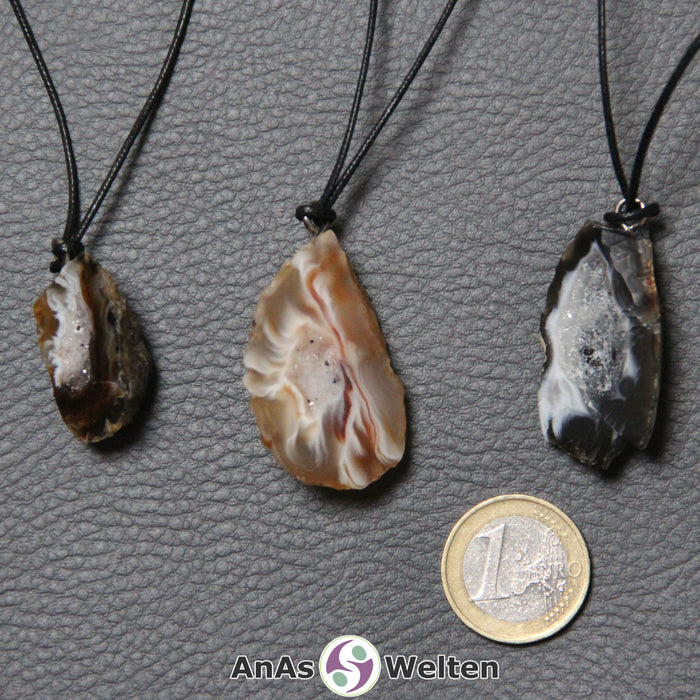 Drei Achat Geoden an einem Baumwollband nebeneinander. Die Steine haben eine schwarze oder braune Farbe.