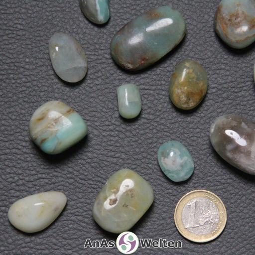 Das Produktbild zeigt den Andenopal Trommelstein in verschiedenen Variationen. Er ist hauptsächlich von hellblauen Farben dominiert und ist oft von Brauntönen durchzogen. Es gibt aber auch Grüntöne und einen weißlichen Rosaton.