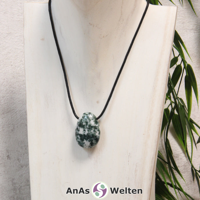 Ein grün-weißer Moosachat gebohrter Trommelstein an einem schwarzen Baumwollband, der um eine helle Büste gehängt wurde.