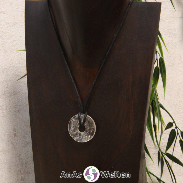 Das Produktbild zeigt einen Bergkristall Donut an einem Baumwollband. Der Edelsteindonut ist farblos, wodurch sich die eingeschlossenen Risse im Inneren in weiß abzeichnen.