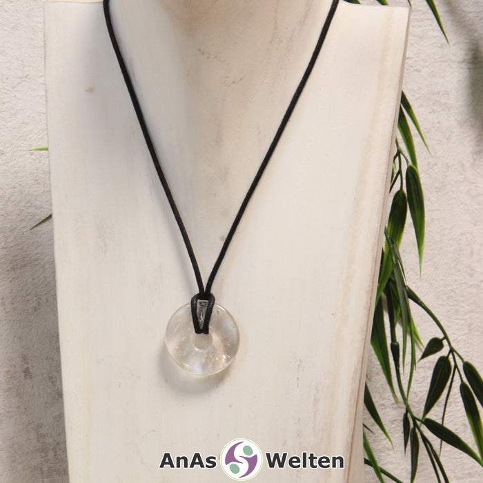 Ein Bergkristall Donut als Kette an einem schwarzen gewachsten Baumwollband um eine helle Büste.