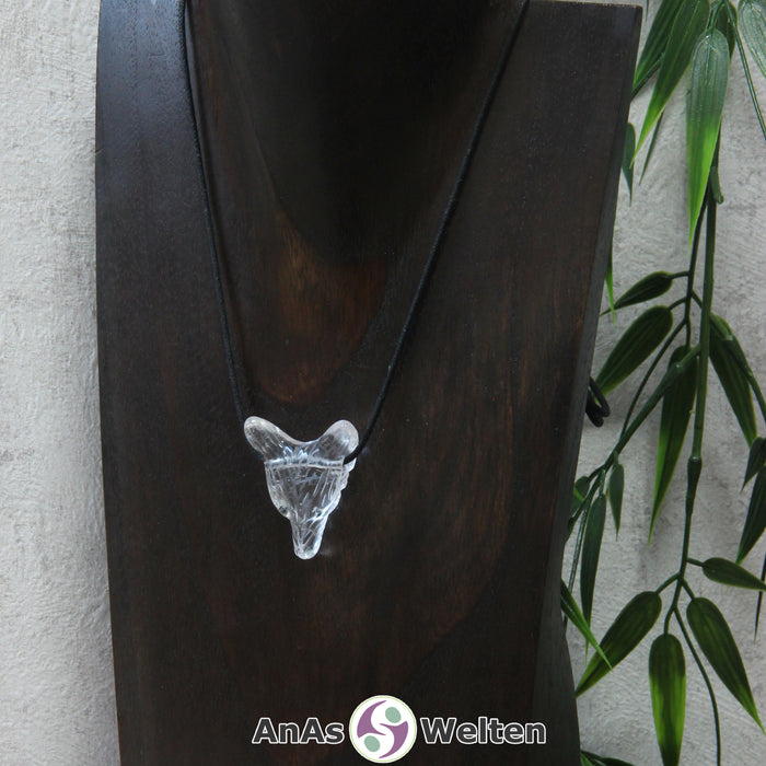 Das Bild zeigt einen Bergkristall Wolf Anhänger an einem Baumwollband. Der Edelstein ist durchsichtig, weshalb man gut die Risse in seinem Inneren erkennen kann. Das Fellmuster und die Nase sind durch kleine Kerben im Edelstein dargestellt. Die Augen sind kleine schwarze Perlen.