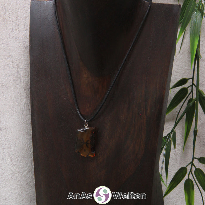 Ein Bernstein Anhänger Fische an einem Baumwollband als Kette um eine dunkle Büste.