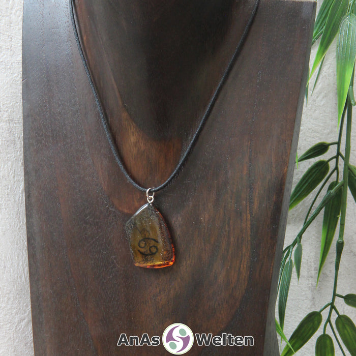 Ein Bernstein Anhänger Krebs an einem Baumwollband als Kette um eine dunkle Büste.