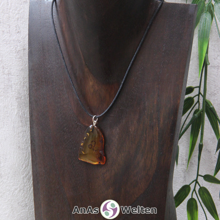 Ein Bernstein Anhänger Löwe an einem Baumwollband als Kette um eine dunkle Büste.