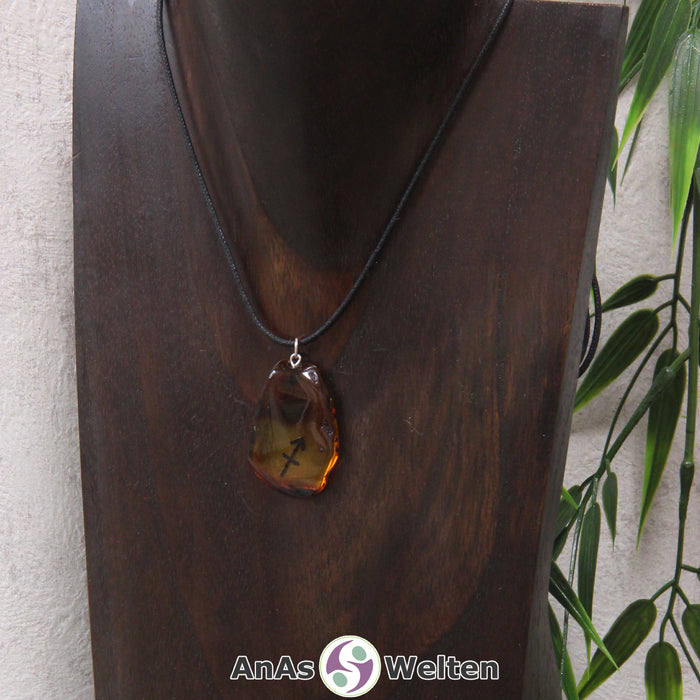 Ein Bernstein Anhänger Schütze an einem Baumwollband als Kette um eine dunkle Büste.
