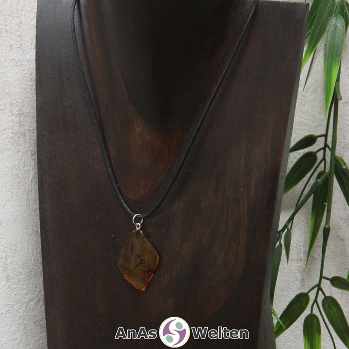 Ein Bernstein Anhänger Steinbock an einem Baumwollband als Kette um eine dunkle Büste.