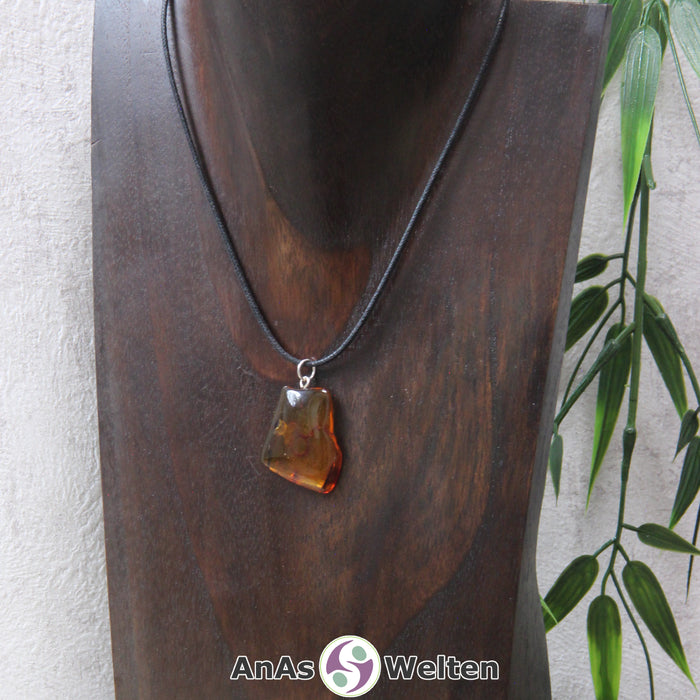 Ein Bernstein Anhänger Stier an einem Baumwollband als Kette um eine dunkle Büste.