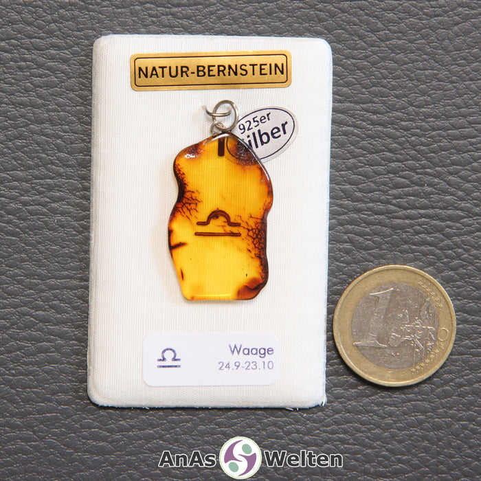 Ein Bernstein Anhänger Waage mit Silberöse an einem Display. Das Sternzeichen ist in den Bernstein eingebrannt.
