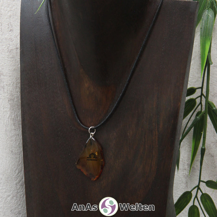 Ein Bernstein Anhänger Waage an einem Baumwollband als Kette um eine dunkle Büste.