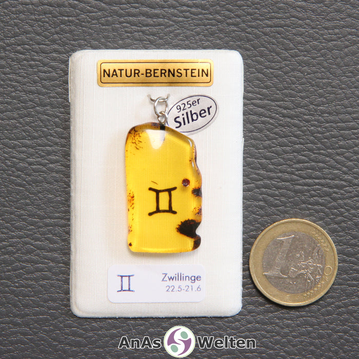 Ein Bernstein Anhänger Zwillinge mit Silberöse an einem Display. Das Sternzeichen ist in den Bernstein eingebrannt.
