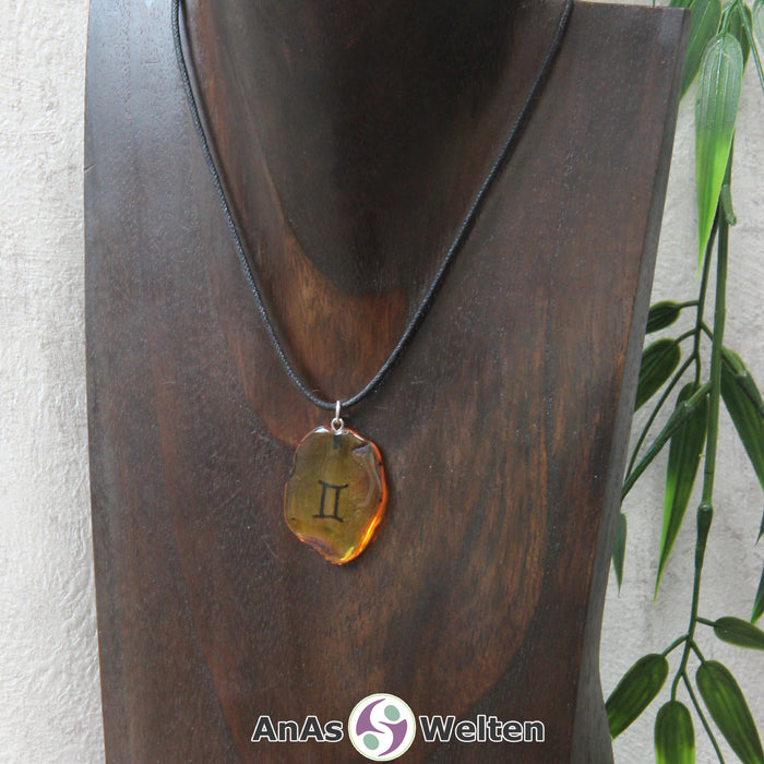 Ein Bernstein Anhänger Zwillinge an einem Baumwollband als Kette um eine dunkle Büste.