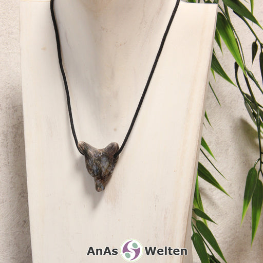 Das Bild zeigt einen Blue Liberty Wolf Anhänger an einem Baumwollband. Der Edelstein hat eine Mischung aus Beige, Braun, Grau und Grau-Blau, die unregelmäßig über den Wolfskopf verteilt ist. Das Fellmuster und die Nase sind durch kleine Kerben im Edelstein dargestellt. Die Augen sind kleine schwarze Perlen.