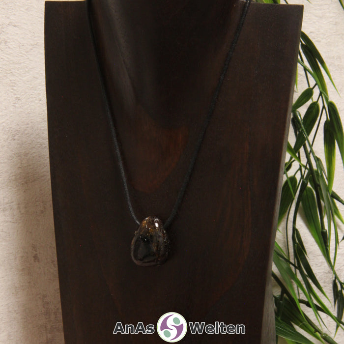 Ein dunkelbrauner Dravit gebohrter Trommelstein an einem schwarzen Baumwollband, der um eine dunkle Büste gehängt wurde.