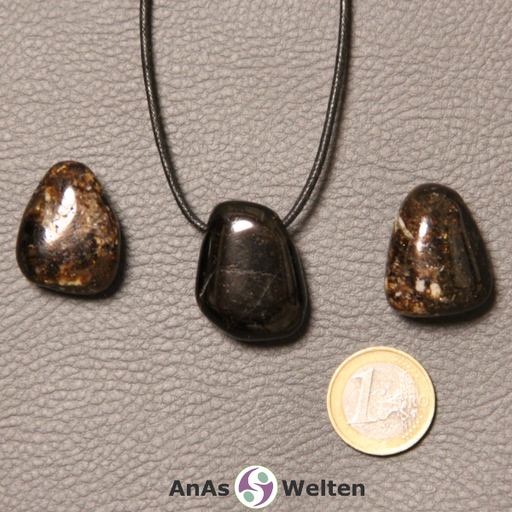 Drei dunkelbraune Dravit gebohrte Trommelsteine nebeneinander. Einer befindet sich an einem schwarzen gewachsten Baumwollband.