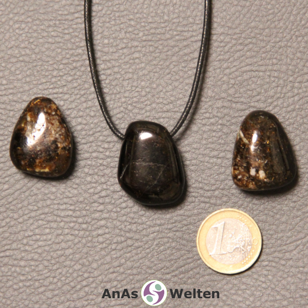 Drei dunkelbraune Dravit gebohrte Trommelsteine nebeneinander. Einer befindet sich an einem schwarzen gewachsten Baumwollband.