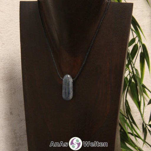 Ein gebohrter Disthen Trommelstein an einem Baumwollband. Der Edelstein hat eine dunkelblaue Farbe. Seine Musterung besteht aus unterschiedlichen unregelmäßigen Dunkelblautönen.