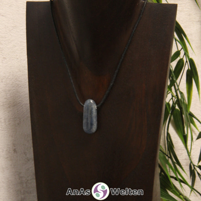 Ein gebohrter Disthen Trommelstein an einem Baumwollband. Der Edelstein hat eine dunkelblaue Farbe. Seine Musterung besteht aus unterschiedlichen unregelmäßigen Dunkelblautönen.