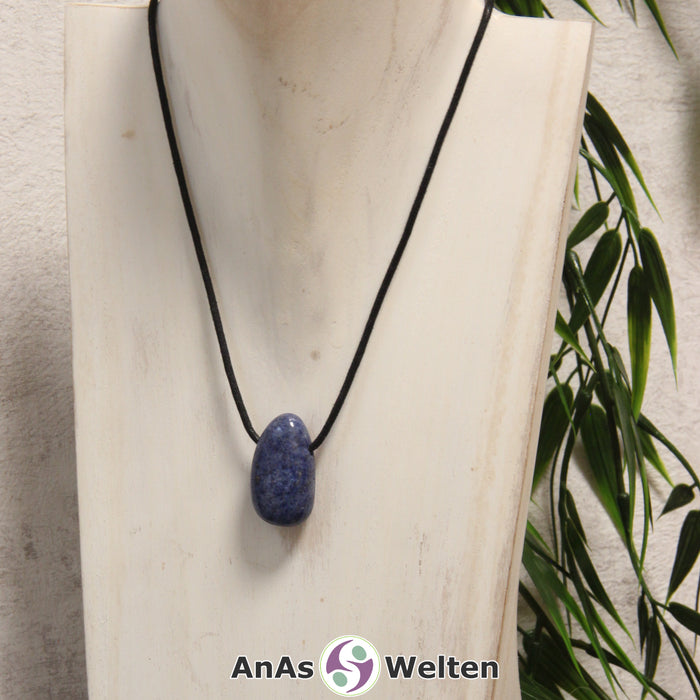 Ein blauer Dumortierit gebohrter Trommelstein an einem schwarzen Baumwollband, der um eine helle Büste gehängt wurde.
