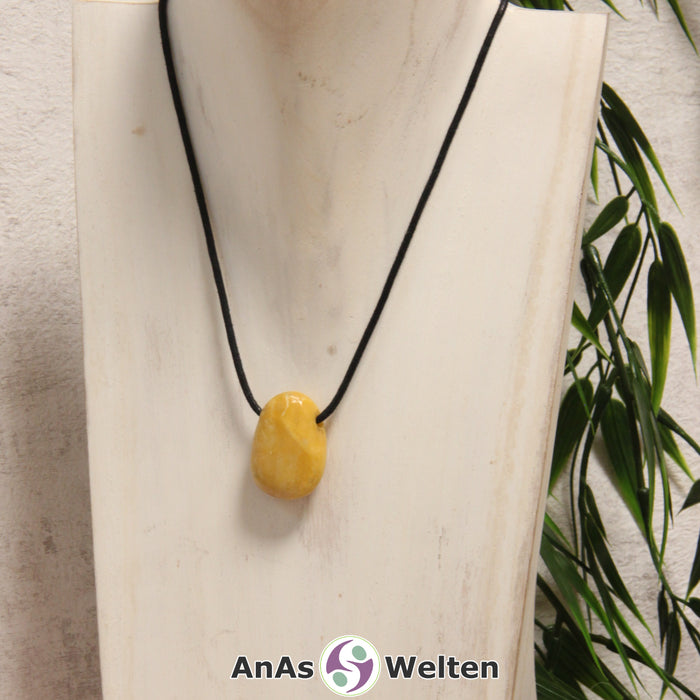 Ein Gelber Jaspis gebohrter Trommelstein an einem schwarzen Baumwollband, der um eine helle Büste gehängt wurde.