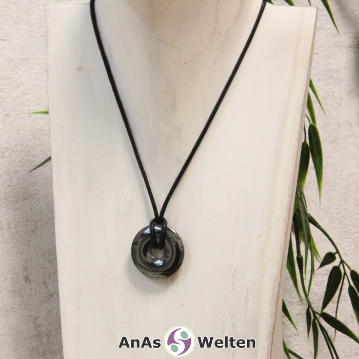 Ein Hämatit Donut als Kette an einem schwarzen gewachsten Baumwollband um eine helle Büste.
